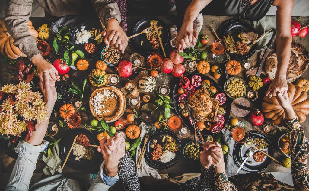 Family or friends praying holding hands at Thanksgiving celebration table